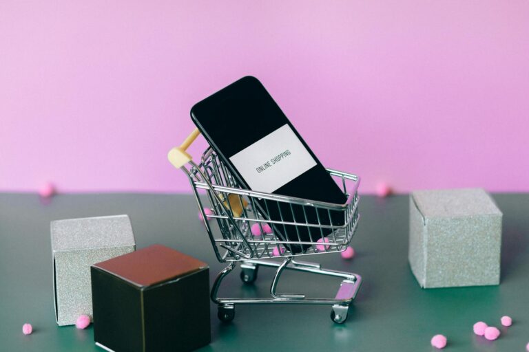 A smartphone with a shopping cart depicting the concept of online shopping in a colorful studio setup.