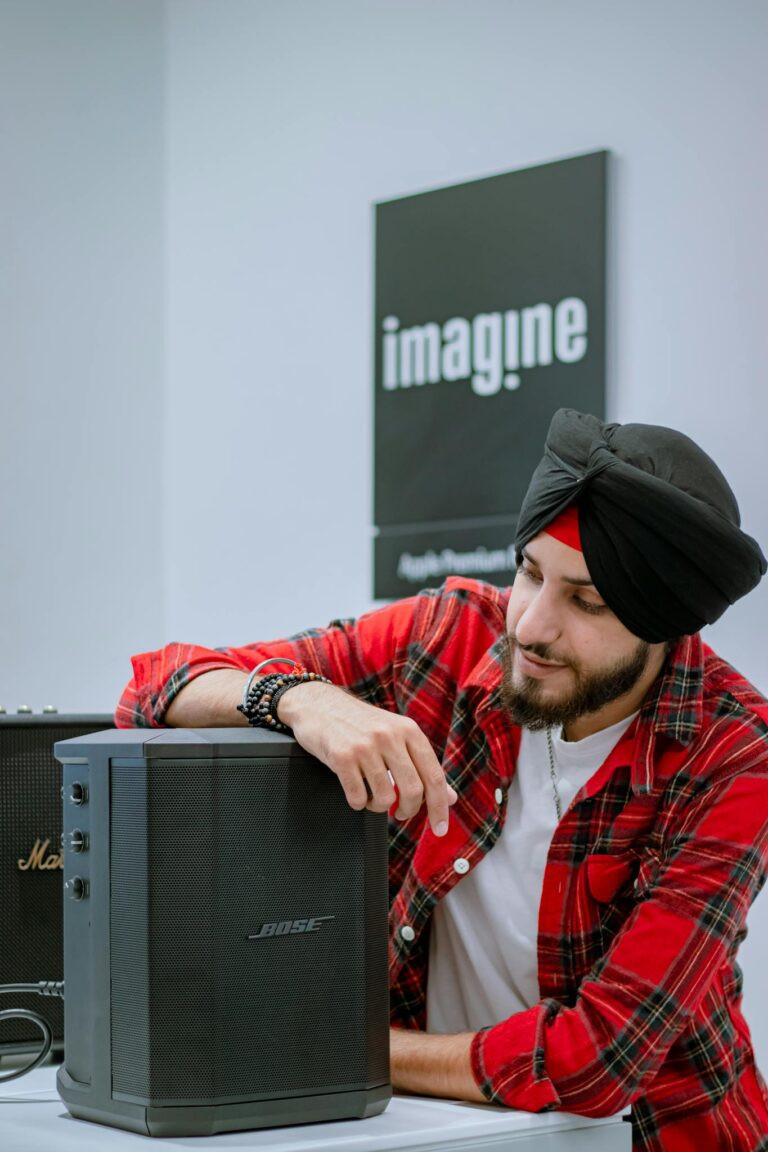South Asian man in plaid shirt examining Bose speaker in electronics shop.